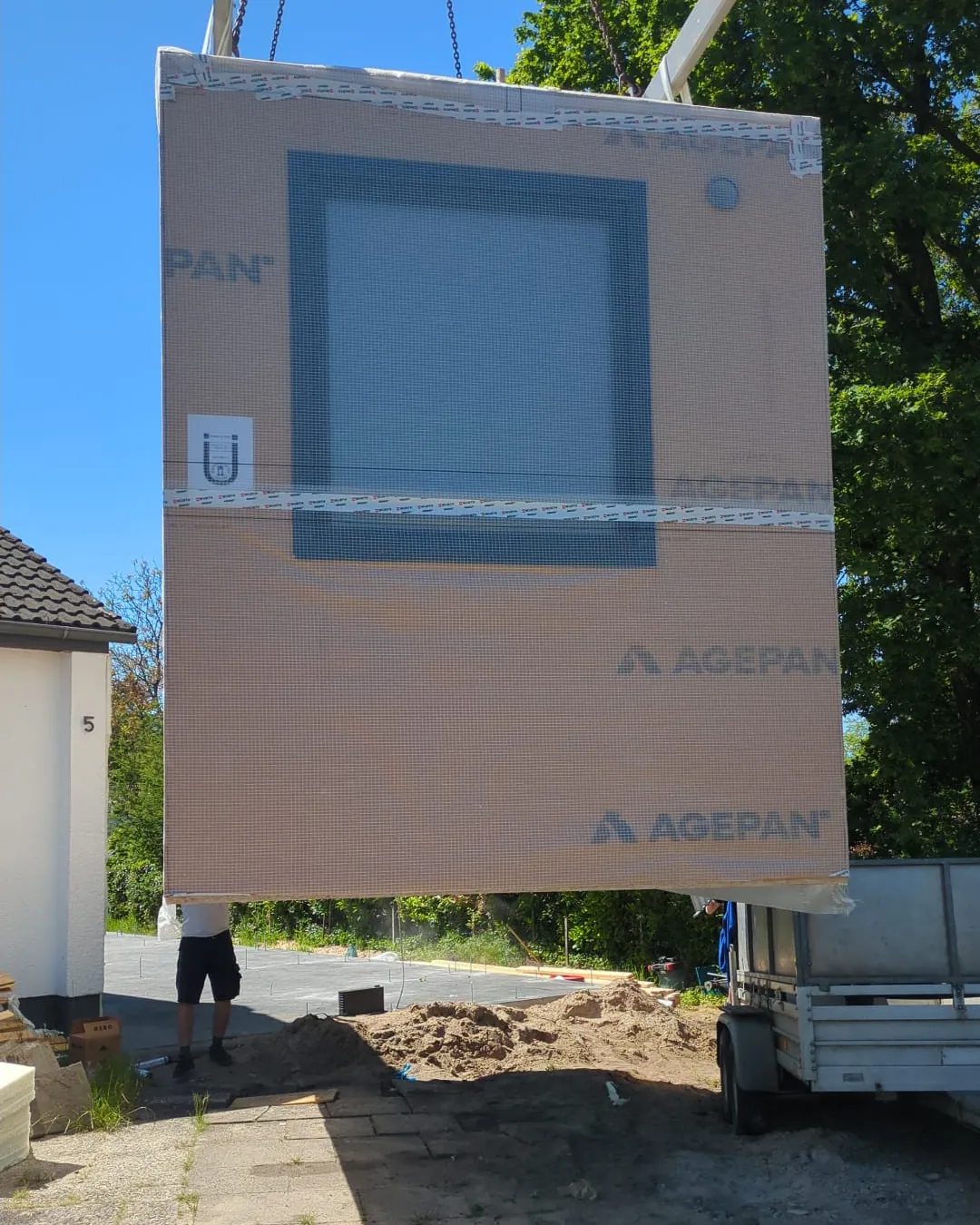 Vorgefertigtes Wandelement hängt am Kran über der Baustelle